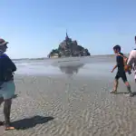Visitors walking on the sandy bay at Mont Saint Michel during a guided day trip from Paris